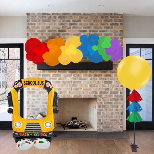 Decorative setup with a school bus, balloons, and colorful paper flowers on a brick wall.
