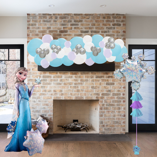 Decorative setup with Elsa figure, balloons, and snowflake decorations in front of a brick fireplace.