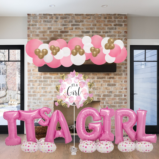 Decorative balloons and signs indicating 'It's a Girl' against a brick wall.