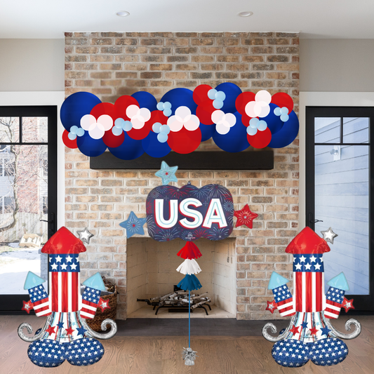 Decorative setup with balloons, 'USA' sign, and festive elements in a room with a brick wall.